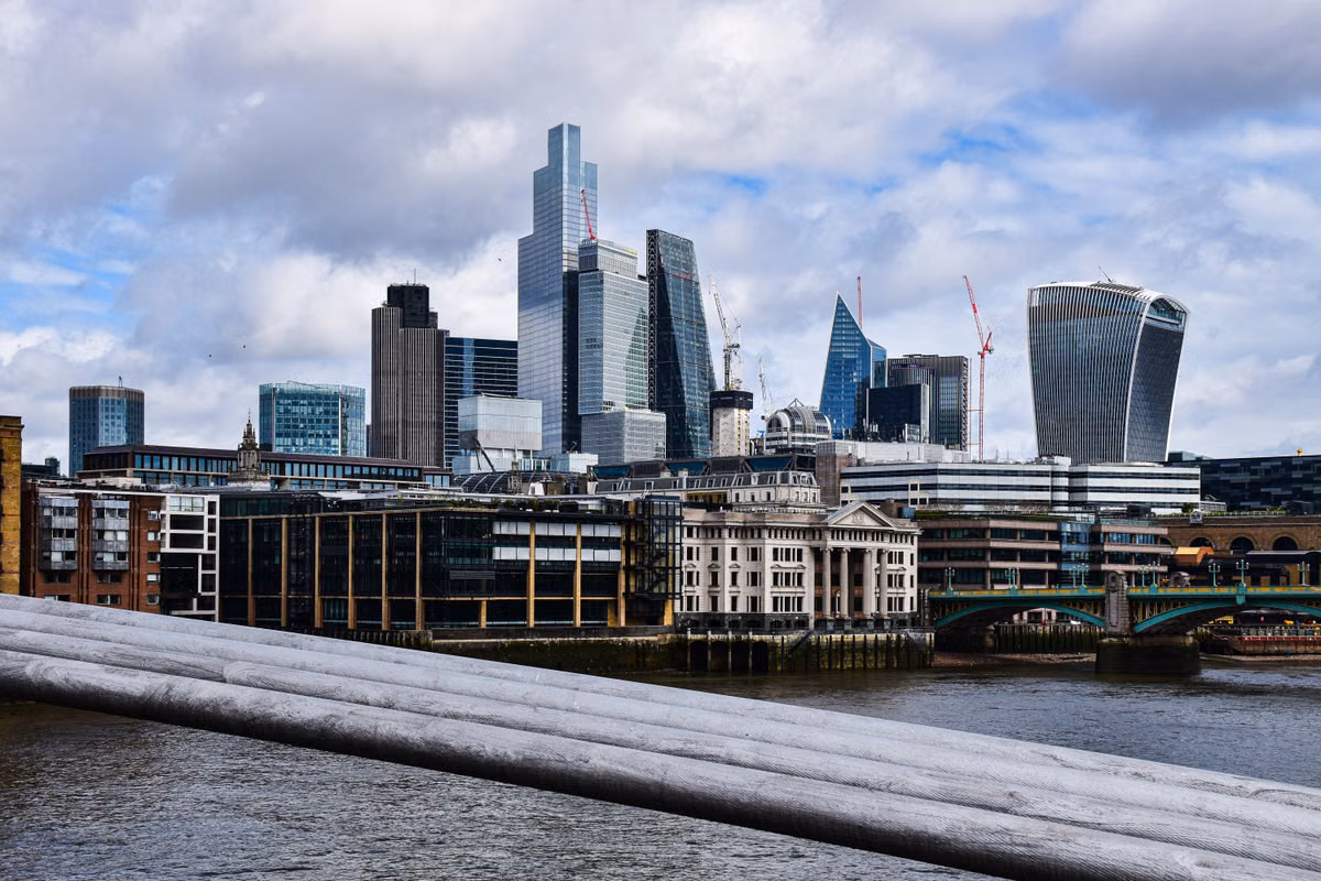 Office towers and tower cranes on the City of London skyline, seen across the River Thames on a cloudy day.